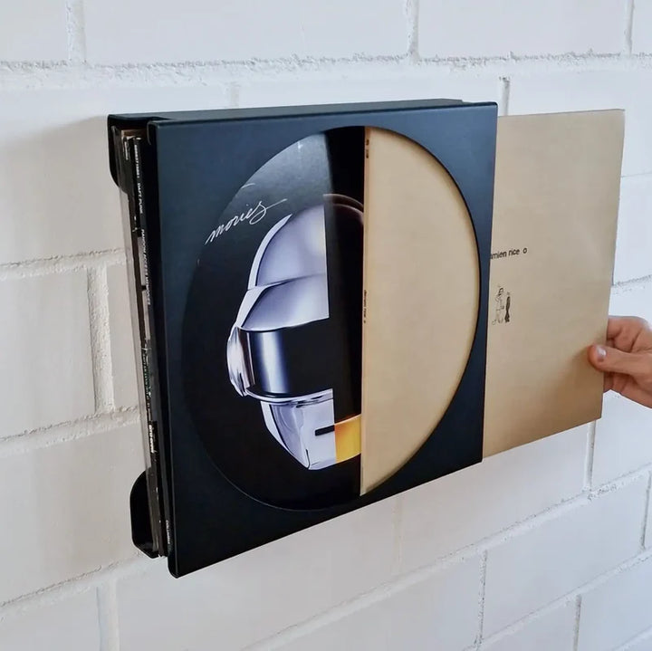 FLATE Schallplatten Wandhalterung Round, Schwarz, an weisser Backsteinwand montiert mit mehreren Schallplatten, eine Hand zieht eine Platte heraus – Coffee Coaching Club