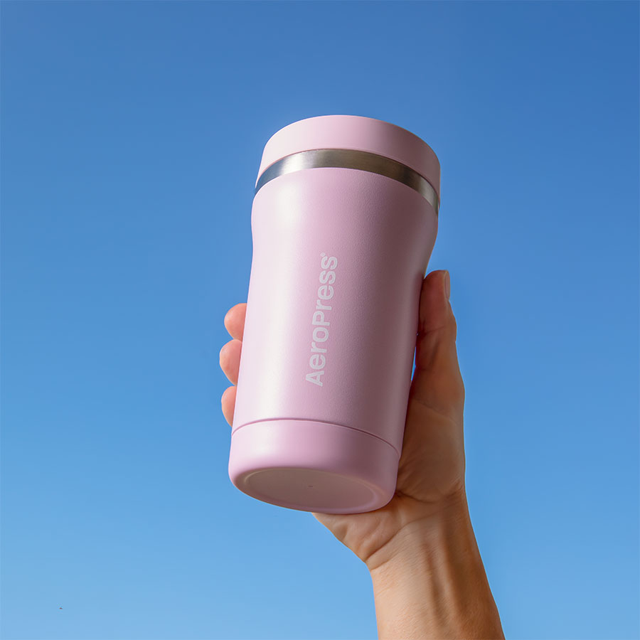 AeroPress Go Plus Travel System - Pink, gobelet tenu à la main sous un ciel bleu - Coffee Coaching Club