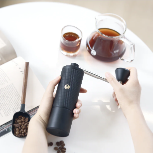 timemore chestnut c5 series handkaffeemühle beim Mahlen in der Hand, im Hintergrund Filterkaffee – Coffee Coaching Club